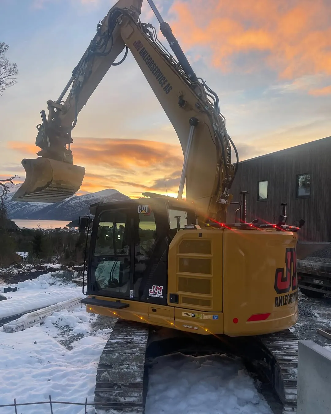 Gravemaskin i solnedgang, med snø på bakken