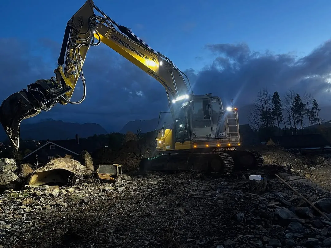 Gravemaskin med arbeidslys i skumringen